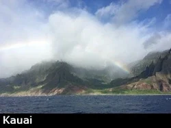 View of Kauai's mountainous Na Pali coast as a rainbow peaks through the clouds and fog from a nearby rain shower