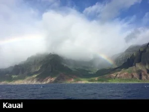 View of Kauai's mountainous Na Pali coast as a rainbow peaks through the clouds and fog from a nearby rain shower