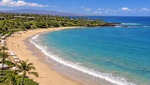 Live view of Kauna'oa beach, as waves break along the shoreline with the rocky, lava point in the background.