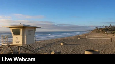 Live view of the beach and Pacific ocean with volleyball courts, fire pits and the lifeguard tower in the foreground.