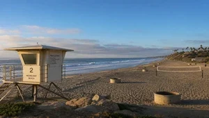 Live view of the beach and Pacific ocean with volleyball courts, fire pits and the lifeguard tower in the foreground.