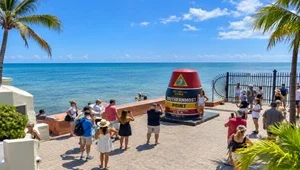 Live view of the people on the boardwalk next to the Southernmost Landmark with the ocean in the background.