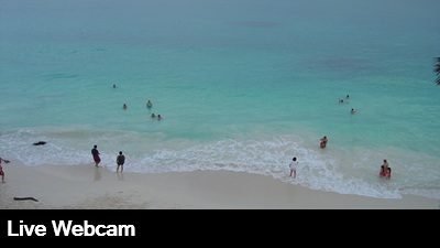 Live view from beach level looking out over the golden sand and Caribbean Sea.