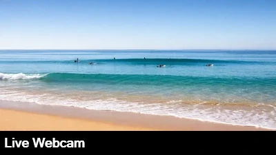 Live close up view of the sand and surf at Waimea Bay in Oahu, Hawaii as surfers wait their turn.